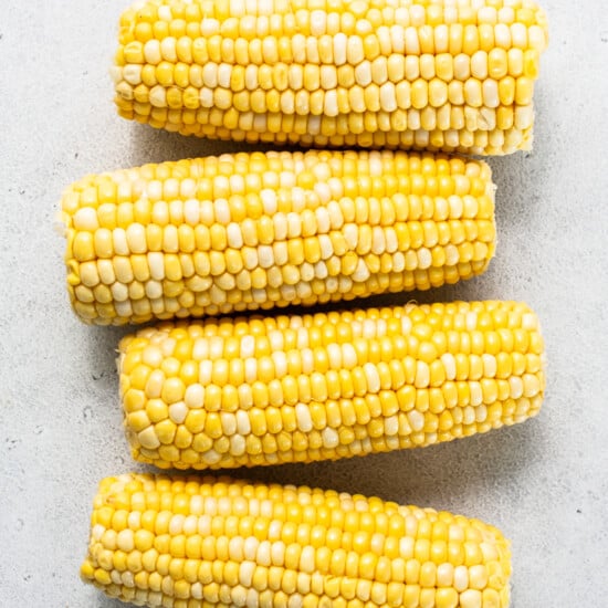 three ears of corn on a white surface.