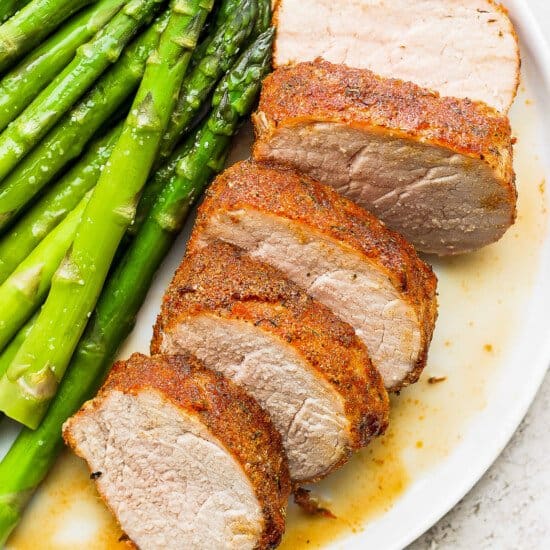 Air fryer pork tenderloin and asparagus on a white plate.