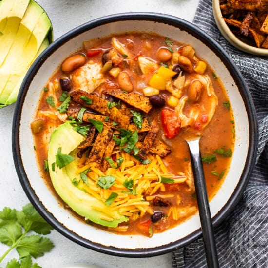 A bowl of mexican chicken soup with avocado and tortilla chips.