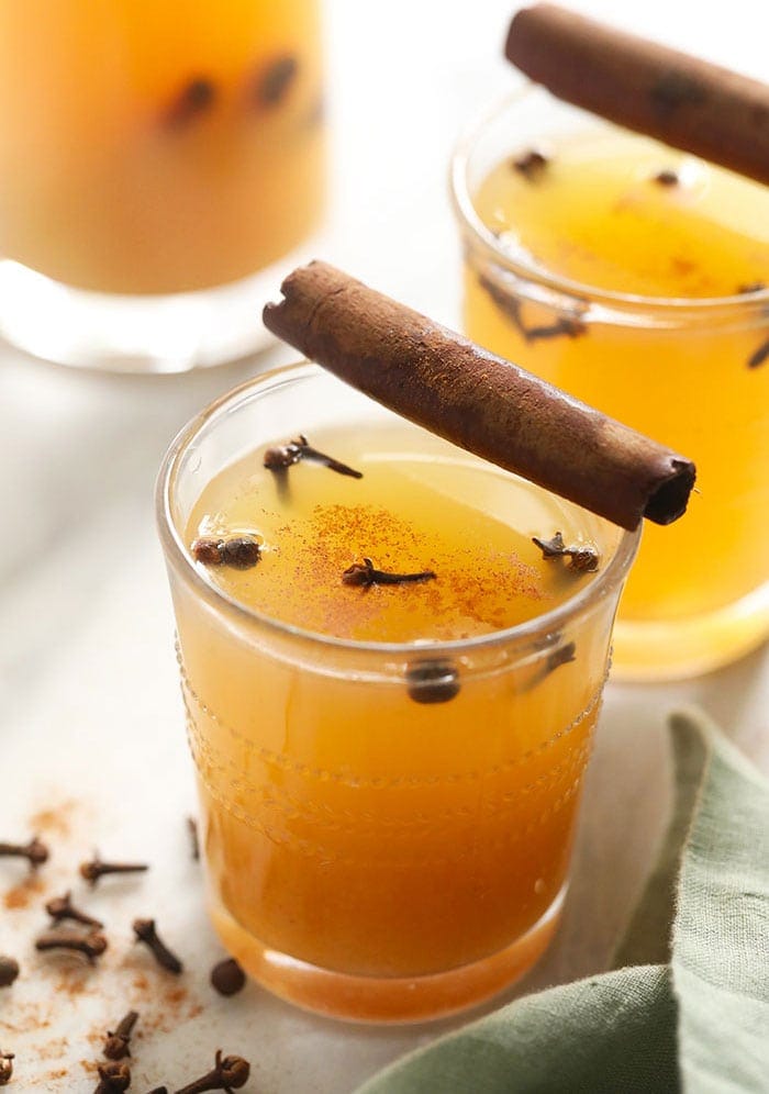 two glasses of apple cider with cinnamon sticks.