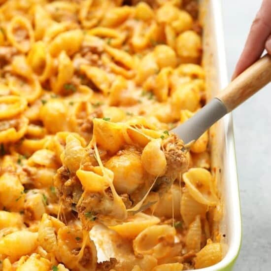 A person scooping hamburger pasta out of a casserole dish.