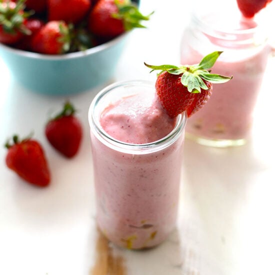 strawberry smoothie with pineapple chunks with strawberry on rim of glass