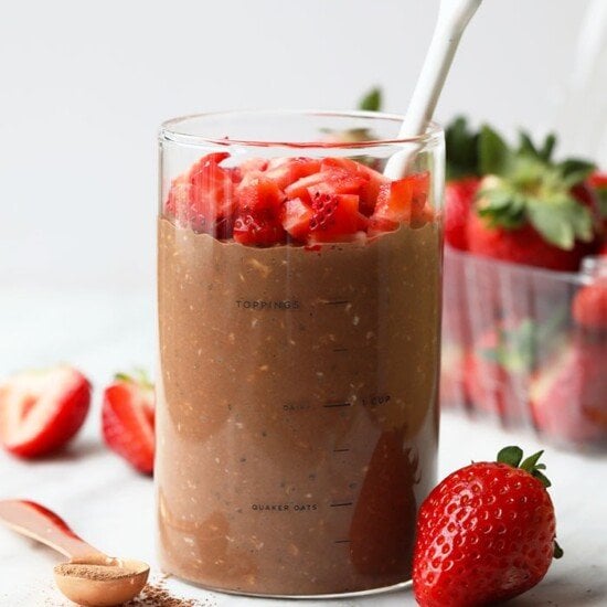 A glass of overnight oats topped with strawberries and a spoon.