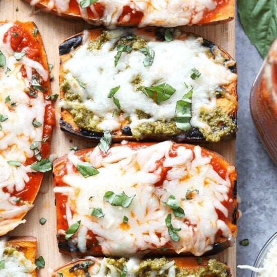 Sweet potato pizzas with pesto and basil garnish on a cutting board.