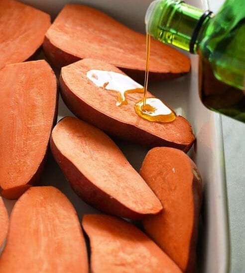 Sweet potatoes bring drizzled with olive oil in a baking dish.